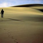 A imagem mostra um homem atravessando um deserto